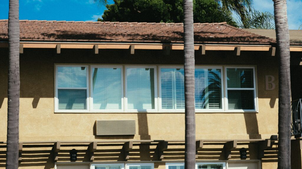 A modern residential building facade with palm trees and clear blue sky.